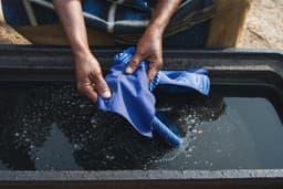 An artisan’s hands lift indigo-dyed adire cloth from a dye pit