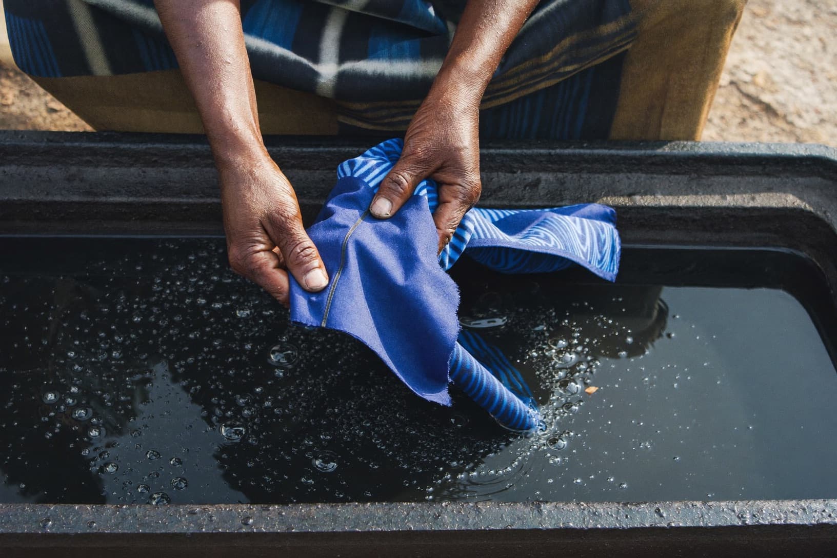 An artisan’s indigo-stained hands lifting dyed adire cloth