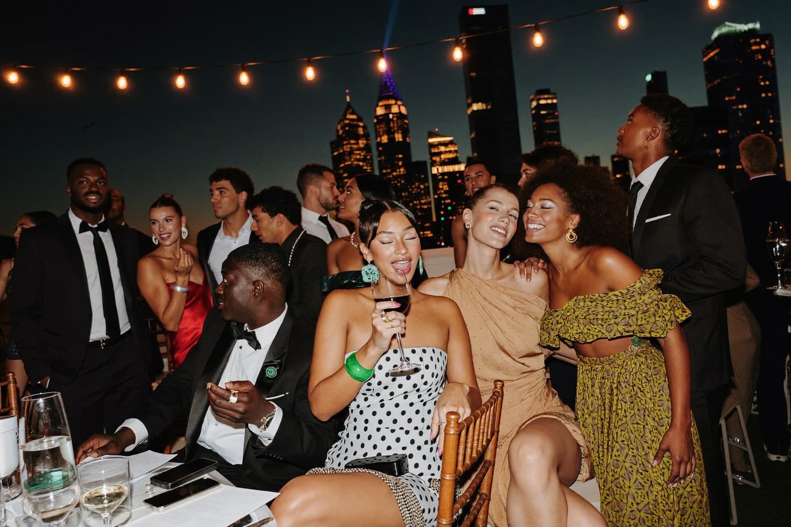 Guests in black tie mingle at a rooftop reception at dusk.