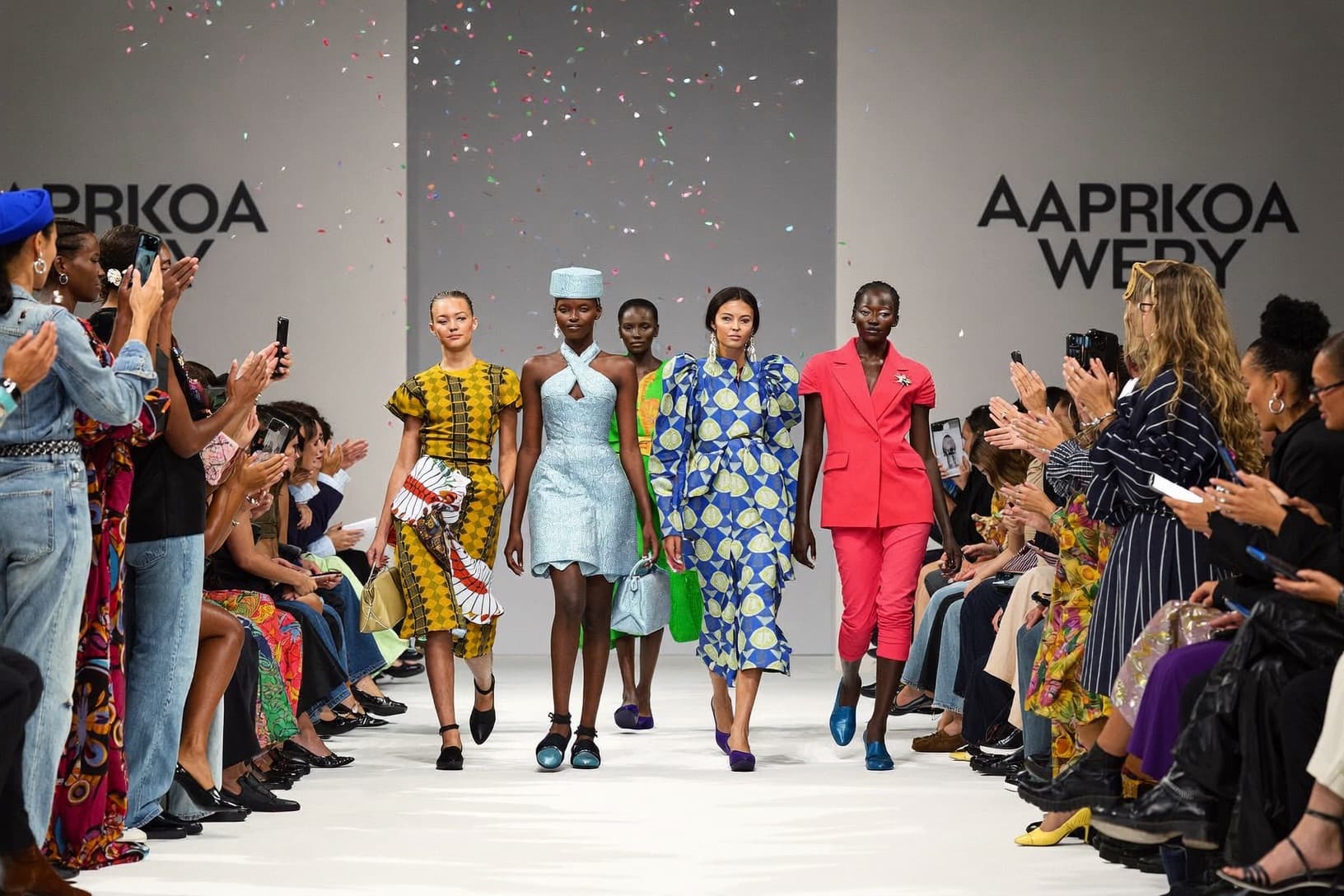 Models walk a runway finale as the audience stands and applauds