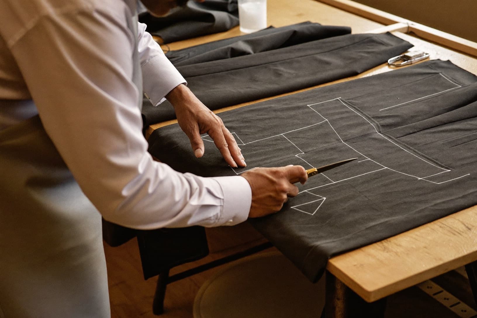 A master tailor cuts suiting cloth at his workbench